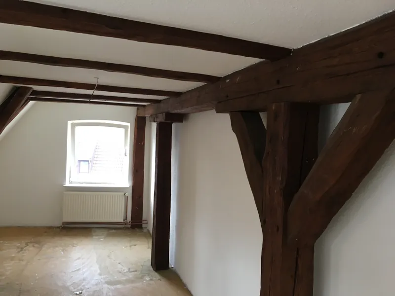 Dachgeschoss mit sichtbaren dunklen Holzbalken und heller Decke