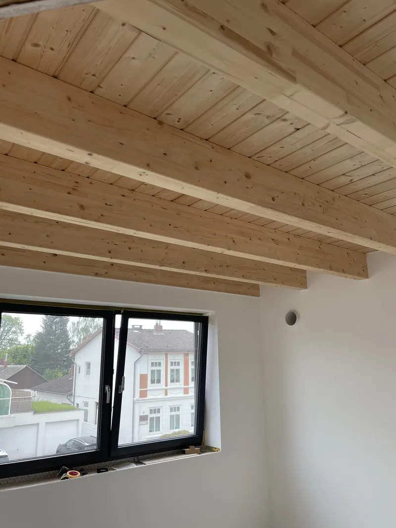 Neue Holzdecke mit sichtbaren Balken über einem hellen Raum