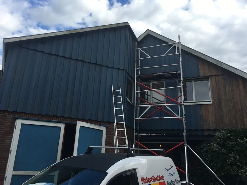 Gewerbehalle mit blauer Fassade, Gerüst und Firmenwagen